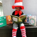 6-7 year old child reading a book with Cat in the Hat hat and socks. 