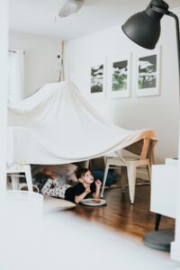 child making a fort or tent from a blanket and eating a sandwich underneath