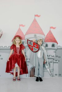 Dress up: a boy dressed as a knight and a girl in old fashioned clothes. Their background is a castle. 