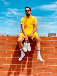 crew socks for men. A man sitting on a wall with his socks visible and holding his shoes