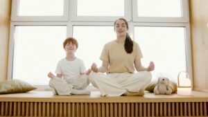 mom and child sitting in the yoga position meditating by a window