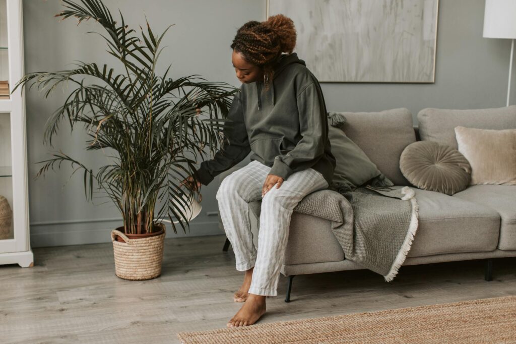 A woman sitting on a couch and watering her pot plant.