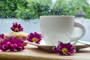 Keep your home clean during the rainy season. A piture of a cup of coffee with flowers next to a rainy window.