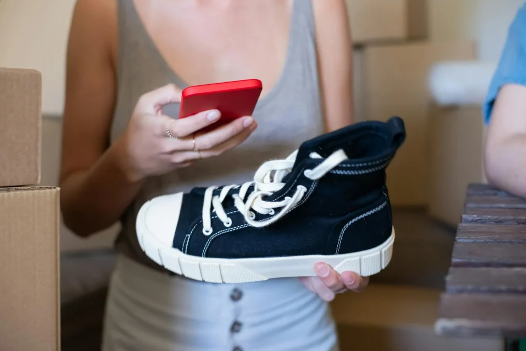 Shopper comparing a sneaker while checking a phone during online checkout.